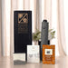 The Blunt Umbrella All Weather Set - A grey umbrella stands beside packaged tea and coffee products, all displayed in a black box, with flowers in the background.