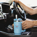 The Hippo 1.2L Mug - A drink bottle in light blue, featuring a handle and a straw, positioned in a car's centre console.