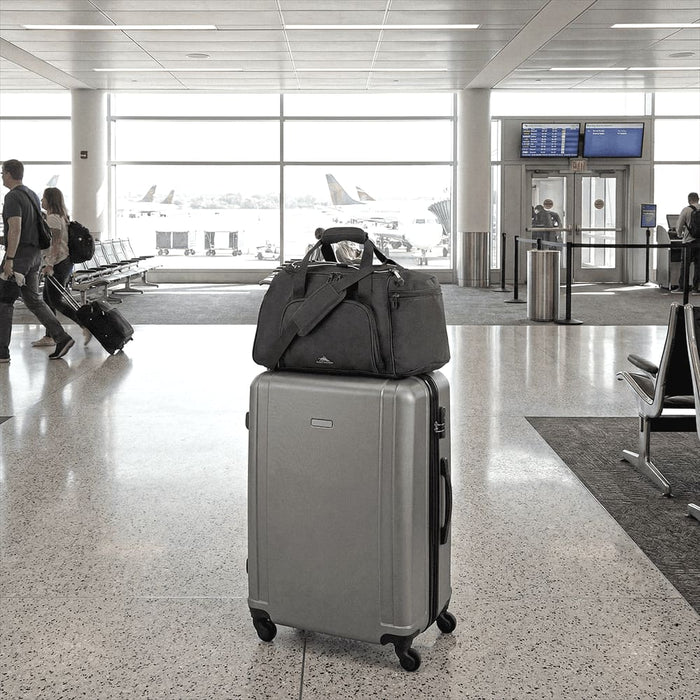 High Sierra Travel Duffel - A grey High Sierra travel duffel rests on top of a silver suitcase in an airport terminal. It features a logo.
