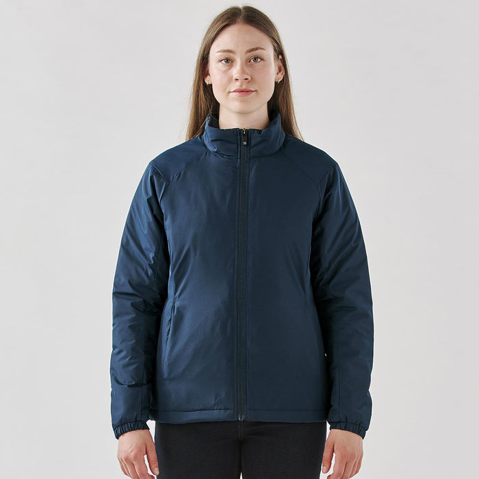 Women's Pacifica Thermal Jacket - A woman wearing a navy blue thermal jacket with a zip front and a high collar, featuring a small logo.