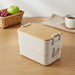 Bamboo Stack & Go Lunch Box - A beige bamboo stackable lunch box with a wooden lid, placed on a wooden surface beside a woven basket and cup.