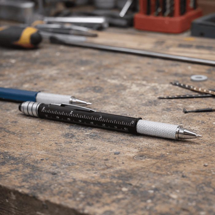 The Balance Pen - A black and silver precision pen lies on a workbench, surrounded by tools and small metal parts.