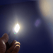 Rechargeable Work Light - A handheld rechargeable work light emits a bright white light against a blue background. It features a logo on its surface.