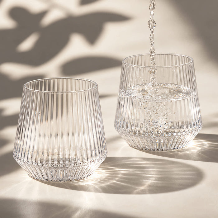 Velora Tumbler by The Line Edit. - A drink bottle featuring a ribbed design, made of clear glass, with water being poured into two glasses.