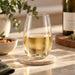 Swift Tumbler - PET 450ml - A drink bottle featuring a clear, curved glass containing white wine, placed on a marble coaster.