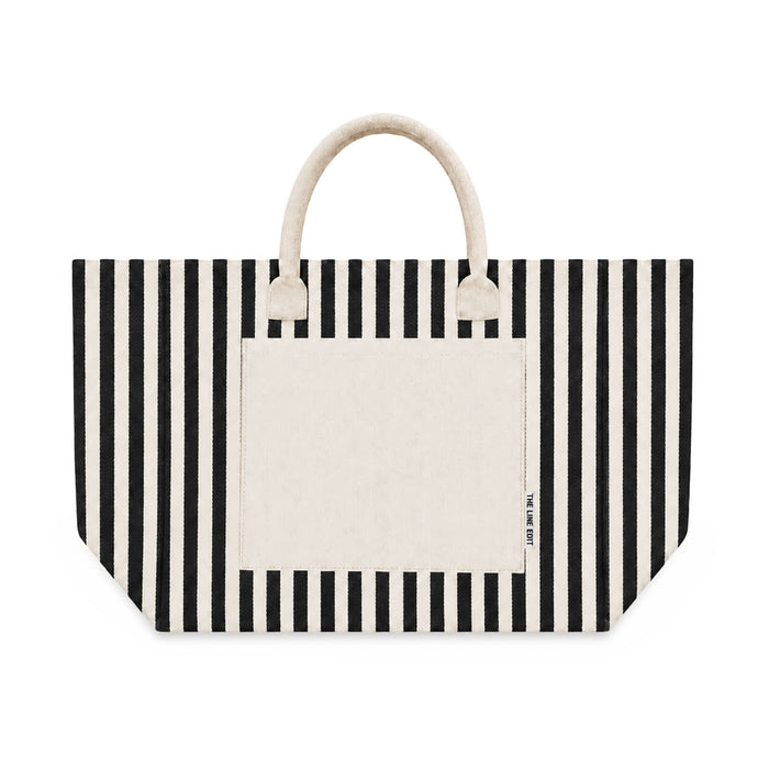 Hampton Tote Bag by The Line Edit. - A striped tote bag featuring black and cream colours, with a solid cream pocket and handles. It has a brand logo.