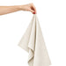 Haven Medium Cotton Tea Towel - A hand holds a light beige cotton tea towel, showcasing its soft fabric and folded design.
