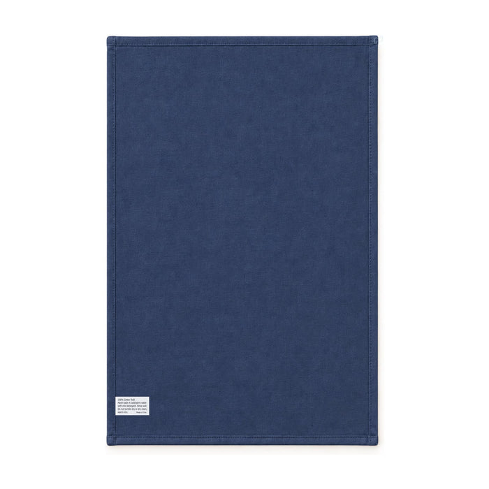 Haven Medium Cotton Tea Towel - A medium cotton tea towel in navy blue with stitched edges and a small tag. It has a simple design and a logo.