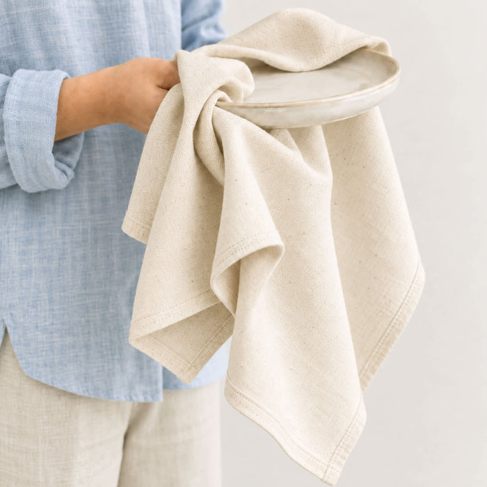 Haven Large Cotton Tea Towel - A large cotton tea towel in a light beige colour, held in one hand alongside a neutral-toned plate.