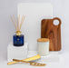 The Host Edit - A collection of homeware items including a blue diffuser, wooden board, gold utensils, and a white candle jar on white pedestals.