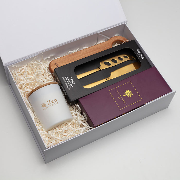 The Host Edit - A gift box containing a ceramic cup, a wooden spoon, and a gold knife set, all arranged with shredded paper.
