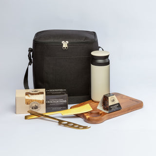 The Carry-On Graze - A black cooler bag, a cream drink bottle, a wooden serving board, gourmet snacks, and a gold cheese knife.