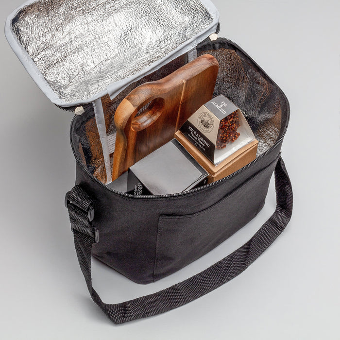 The Carry-On Graze - A black cooler bag with a silver insulated interior, containing a wooden cutting board and packaged food items.