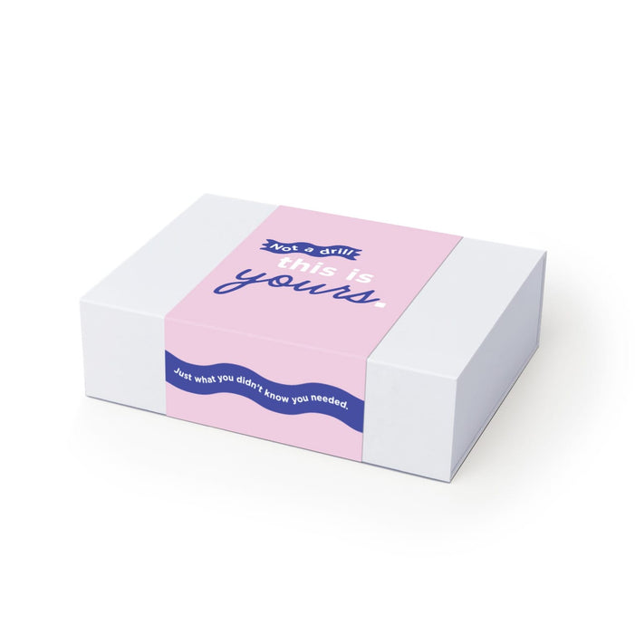 The Ultimate Welcome - Hot Chocolate Edition - A white box with pink and blue design featuring a logo. The text includes playful phrases and a wrap-around band.