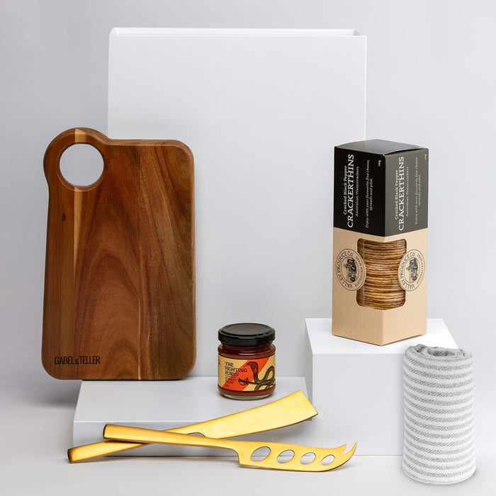 The Nibble Set - A wooden cheese board, gold cheese knives, a jar of spread, coasters, and a coiled rope on a white background.