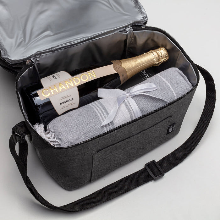 Bubbles & Beachdays - A cooler bag in grey, containing a bottle of champagne and a blanket, with a shoulder strap and a front pocket.
