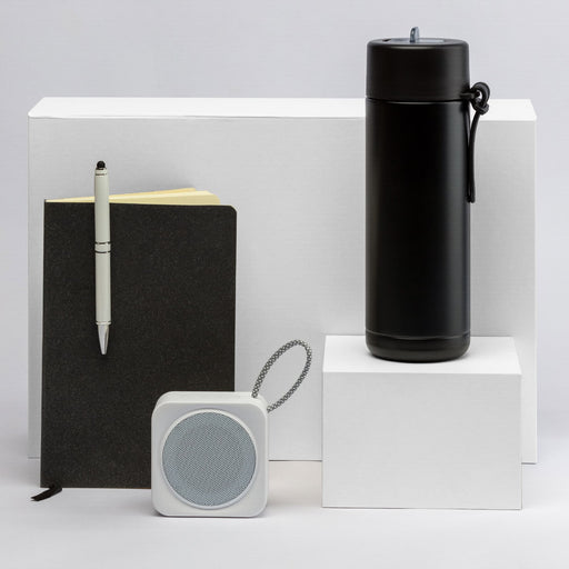 The Daily Setup - A black drink bottle, a black notebook, a white speaker, and a pen displayed on white pedestals.