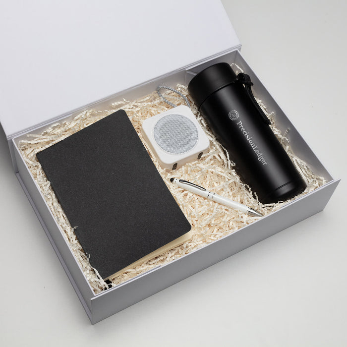 The Daily Setup - A black drink bottle, notebook, white speaker, and pen in a gift box with shredded paper filling.