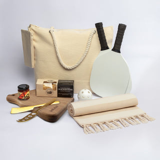 The Sunchaser Set - A cream tote bag, wooden board, drink jar, cheese knife, paddles, ball, picnic blanket, and gourmet snacks.