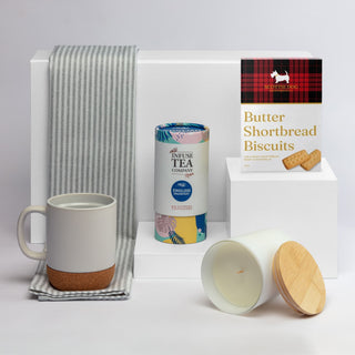 The Brew Ritual - A coffee mug in grey and cork, a tea canister, a candle with a wooden lid, and shortbread biscuits, arranged on a white background.