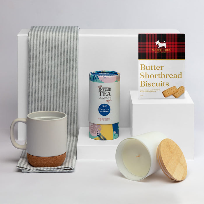 The Brew Ritual - A coffee mug in grey and cork, a tea canister, a candle with a wooden lid, and shortbread biscuits, arranged on a white background.