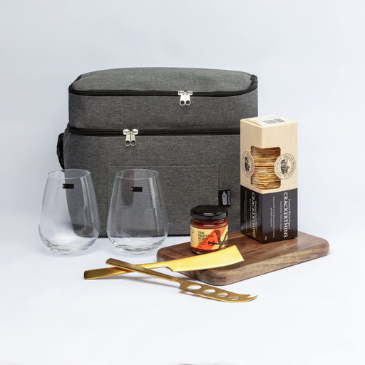 The Refined Graze - A grey cooler bag with two drinking glasses, a jar of preserves, gourmet crackers, and a wooden serving tray with a gold knife.