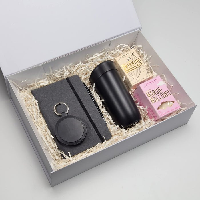 The Ultimate Welcome - Hot Chocolate Edition - A travel mug in black, a notebook, a keyring, and marshmallows in a gift box with shredded fill.