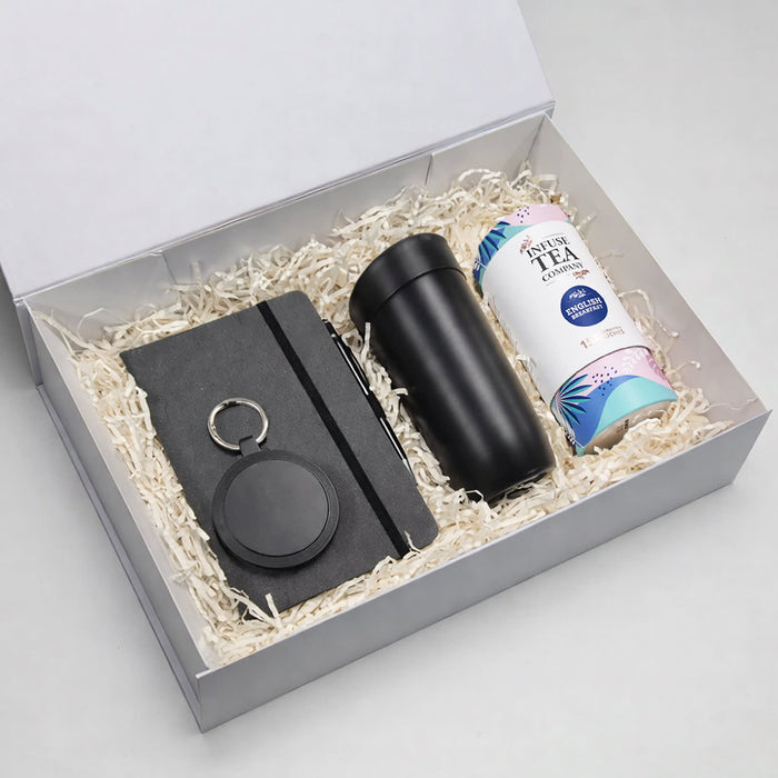The Ultimate Welcome - Tea Edition - A gift box contains a black drink bottle, a notebook, a keyring, and a canister of tea, all nestled in shredded paper.