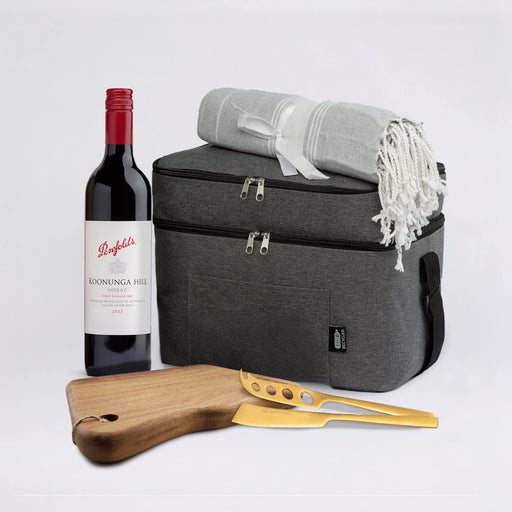 The Sunset Pour - A grey cooler bag with a red wine bottle, a grey blanket, and a wooden cheese board with a gold cheese knife.