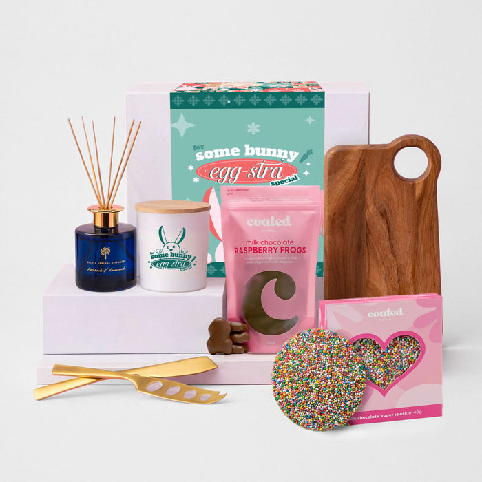 The Generous Host - A gift box featuring a wooden cheese board, chocolate bag, candle, diffuser, and a decorative sprinkle cookie.
