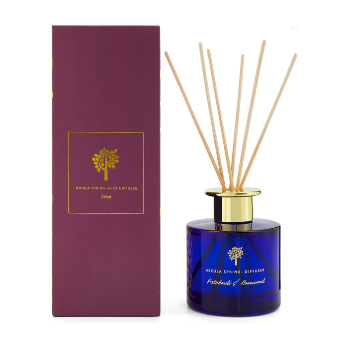The Generous Host - A reed diffuser with a blue glass bottle, gold lid, and bamboo reeds, packaged in a purple box.
