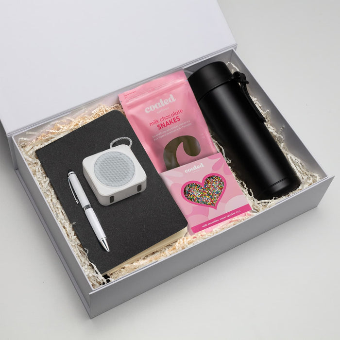 The Sweet Setup - A gift box containing a black drink bottle, notebook, pen, speaker, and pink chocolate snakes.