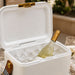 Pavilion Cooler by The Line Edit. - A white cooler filled with ice and a bottle of wine, featuring a gold latch and a striped handle.