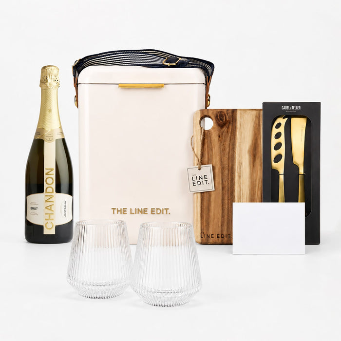 The Pour & Gather Hamper - A champagne bottle, insulated bag, wooden chopping board, knife set, two glasses, and a blank card. The colours are neutral and earthy.