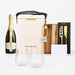 The Pour & Gather Hamper - A champagne bottle, insulated bag, wooden chopping board, knife set, two glasses, and a blank card. The colours are neutral and earthy.