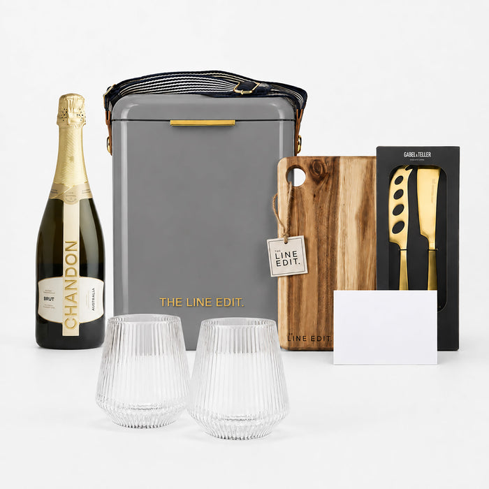 The Pour & Gather Hamper - A grey insulated hamper containing a bottle of sparkling wine, two glass tumblers, a wooden cutting board, and a knife set.