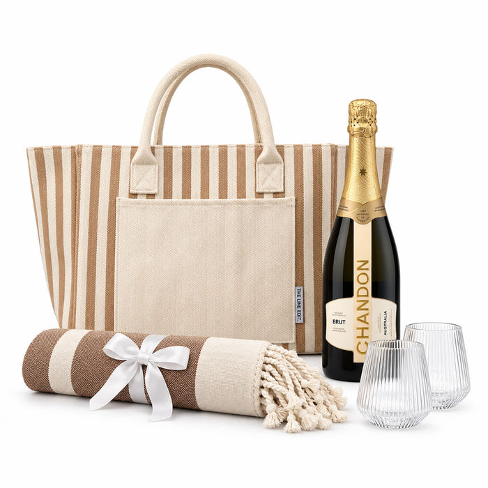 The Sun & Sip Gift Set - A striped tote bag, a bottle of champagne, two glasses, and a rolled blanket with a ribbon.