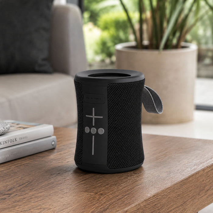 Delta 8W Speaker - A black portable speaker with buttons on the front, placed on a wooden table beside a book and a plant.
