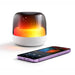 Dazzle RGB Speaker - A Dazzle RGB Speaker in white with a glowing gradient light beside a smartphone displaying music controls.