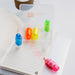 Mackie Highlighter Sets - A transparent case containing four highlighters in blue, orange, yellow, and pink, placed on a notepad with lines.