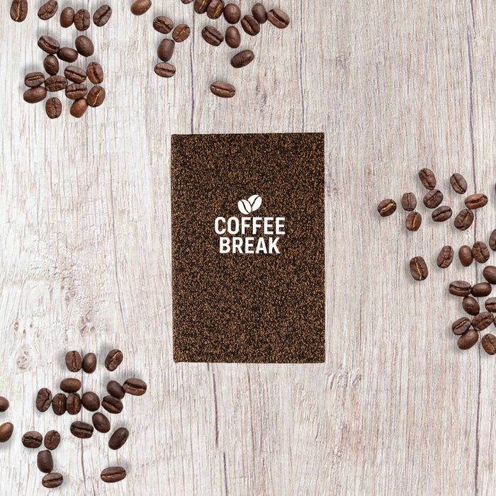 Coffee Grounds A6 Notebook - A brown A6 notebook surrounded by coffee beans on a wooden surface, featuring a logo on the cover.
