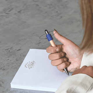 Harley Bamboo Spinner Pen - A wooden pen with a blue grip is being held over a blank notepad on a textured surface.
