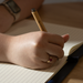 SunScribe Notebook (A4) - A hand holding a pen writes in a lined, cream-coloured notebook on a wooden surface.