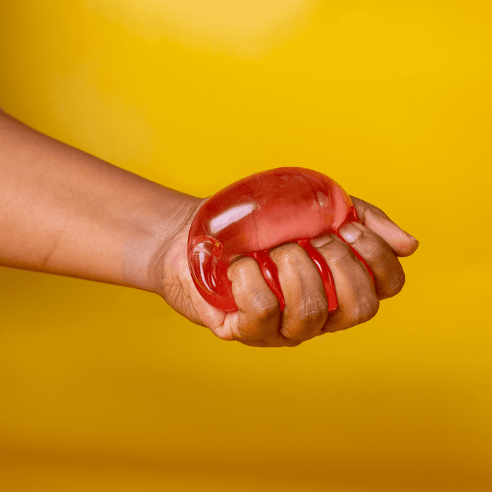 Jelly Cube Sensory Toy - A hand squeezing a translucent red jelly cube sensory toy against a bright yellow background.