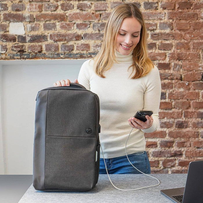 Swissdigital Arosa Backpack - A grey Swissdigital Arosa Backpack with a logo, placed beside a laptop, while a person is using a smartphone.