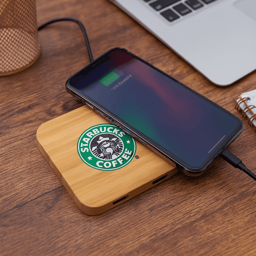 Trafalgar Bamboo charging dock - A bamboo wireless charging dock with a phone on top, featuring a logo and placed on a wooden surface.