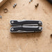 Trekk Multifunction Tool - A silver and black multifunction tool displayed on a wooden surface, surrounded by small screws and metal fragments.