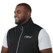 Men's Joris Eco Waterproof Softshell Vest - A black men's softshell vest with a high collar and a logo on the front, worn over a grey shirt.