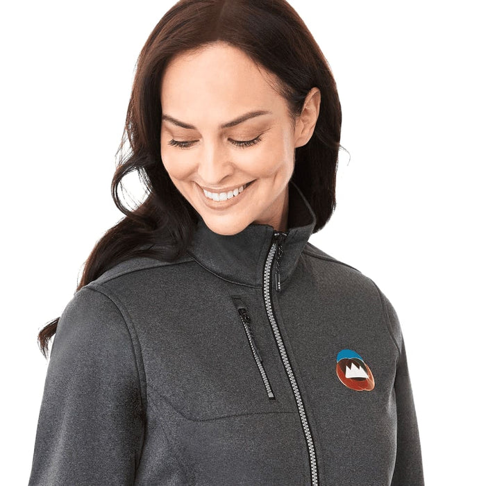 Women's Joris Eco Waterproof Softshell Jacket - A woman in a grey softshell jacket with a logo, featuring a high collar and zippered pockets.