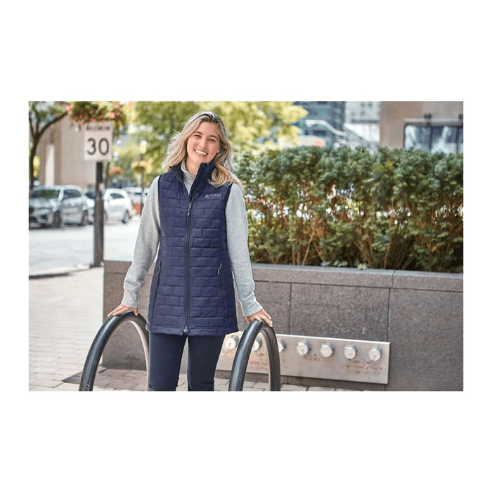 Women's Telluride Lightweight Packable Insulated Puffer Vest - A woman wearing a navy insulated puffer vest over a grey top, standing outdoors with greenery in the background.